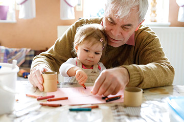 cute little baby toddler girl and handsome senior grandfather painting with colorful pencils at home