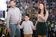 © LIGHTFIELD STUDIOS - happy young family pointing with finger and looking away in bicycle shop