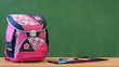Pink girly school bag and pencil case on a desk against greenboard. First day of school concept.
