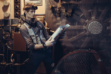 Portrait Of A Young Mad Scientist Traveler In A Steampunk Style Suit With A Card.
