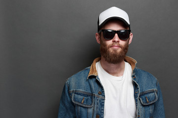 Hipster handsome male model with beard wearing white blank t-shirt and a baseball cap with space for your logo or design in casual urban style