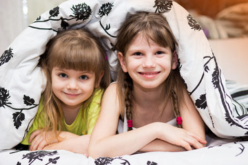 funny little sisters hides under blanket. cute girls having fun on bed. concept of kids sleep, care 