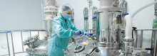 Pharmaceutical Factory Woman Worker In Protective Clothing Operating Production Line In Sterile Environment