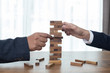 Two Businessman hands play wood block tower game.