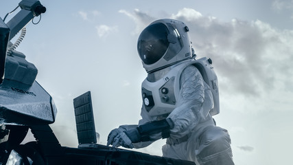 Wall Mural - astronaut in the space suit works on laptop, adjusting rover on a new alien planet. day light high-t