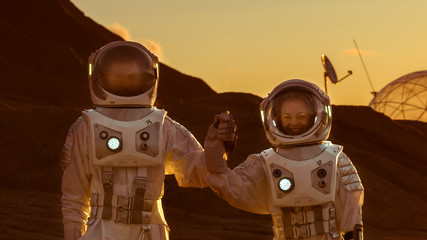Wall Mural - two astronauts wearing space suits holding hands on mars/ red planet. love in space travel, explorat