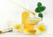Honey spa treatment. Pouring sweet golden honey to jar, plumeria flowers, soft sunny light. Natural homemade skincare.