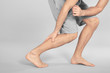 © New Africa - Young man suffering from pain in leg on grey background