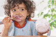 © JPC-PROD - Toddler sitting in highchair and eating greek yogurt. Baby learning to eat and has yogurt on face and hair