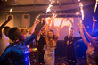 © Seventyfour - Group of cheerful friends holding Bengal lights in hands and dancing to trendy music while celebrating New Year on dance floor of modern night club