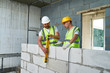 © Seventyfour - Portrait of two construction workers wearing hardhats and reflective vests  checking concrete block wall using level, copy space