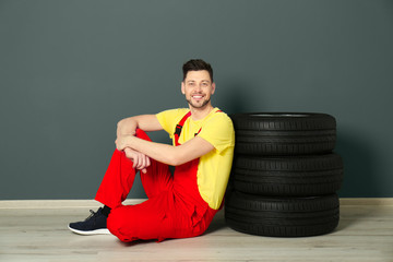 Poster - Male mechanic with car tires on color wall background