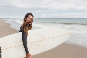 young adorable woman with long hair and sportive tanned body, smiling and jogging with surf board on