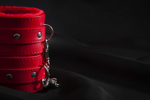 Bondage, Adult Sex Games And BDSM Lifestyle Concept With Close Up On A Pair Of Red Leather Handcuffs On Black Silk With Copy Space
