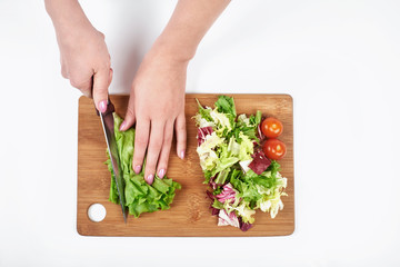 Closeup of woman cook's hands slicing salad and vegetables on a wooden board, isolated on white background