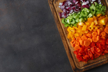 Canvas Print - Chopped fresh vegetables arranged on cutting board on dark background with copy space, top view