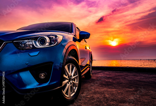 Fotomural Blue compact SUV car with sport and modern design parked on concrete road by the sea at sunset