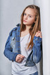 Fashion portrait girl near white wall.Stylish beautiful teenager model clothed in urban casual clothes,jeans jacket. Girl blonde adolescent 11 years posing looking confident,serious face. Model tests.