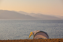 Small Shelter On Shores Of Mountain Lake With Mountains Silhouettes On Horizon At Sunset