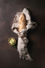 Loaf Of Fresh Baked Artisan Baguette Bread In Linen Cloth With Butter And Herbsover Dark Brown Texture Background. Top View, Copy Space.