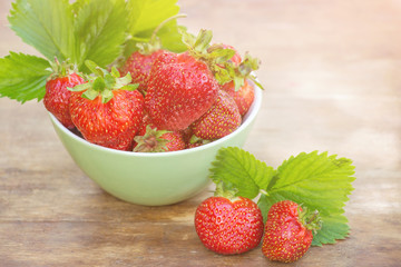 Fresh organic strawberries with green leaves in a bowl closeup