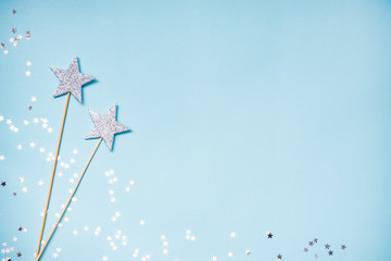 Two silver party magic wands and scattered sequins on a blue background. Copy space.