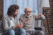 © LIGHTFIELD STUDIOS - adult son and senior father talking on sofa at home