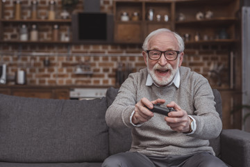 happy handsome grey hair man playing video game at home