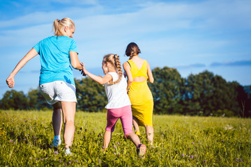  Zwei Frauen und ein Mädchen spielen auf einer Sommerwiese