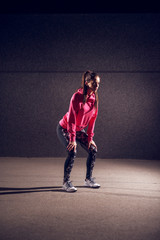 Wall Mural - Portrait vertical view of young athletic slim fashion active girl crouching while having a break on the street in front of the grey wall at night.