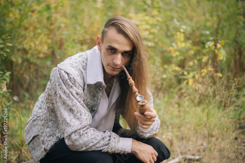 Sexy Long Haired Man With A Pipe In His Hands In The Woods In A