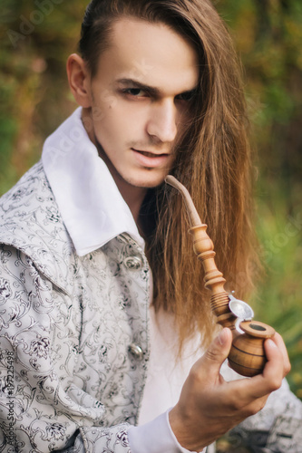 Sexy Long Haired Man With A Pipe In His Hands In The Woods In A