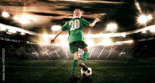 Plakat Dziecko - piłkarz. Chłopiec naprzód w futbolowym sportswear na stadium z piłką. Pojęcie sportu.