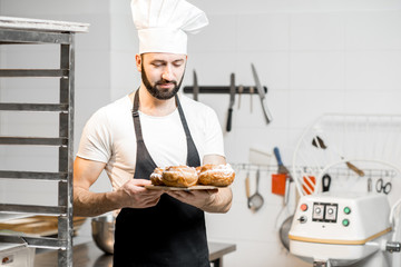 Portrait of a handsome confectioner stnading with sweet pastry in the professional kitchen