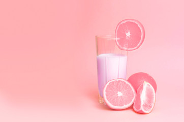 A glass with pink orange juice with the cut oranges on a pink background. Juicy color scale, pin up, pop up styles. Food for breakfast, a healthy drink with vitamins and miniroalami. A sunny drink.