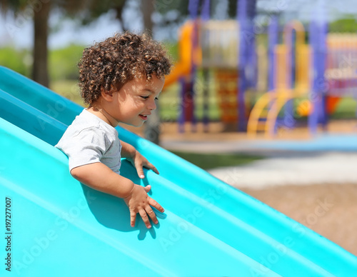 Young Boy With Curly Hair Has Fun As He Goes Down A Slide At A