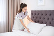 Young maid making bed in hotel room
