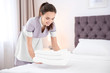 Young maid with stack of towels in hotel room