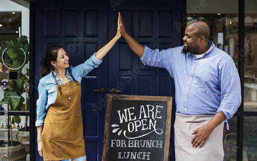 Fotomural Cheerful business owners standing with open blackboard