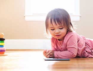 Wall Mural - Happy toddler girl playing with her tablet computer in her house