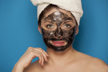 Young beautiful woman with towel on her head posing with black mask on her face