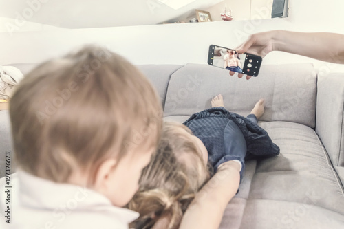 Two Children Lie On The Couch And Looking At A Smartphone Buy