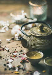 Traditional Asian tea ceremony arrangement. Iron teapot, cups, blooming almond flowers, dried rose buds and candles over wooden table background, selective focus