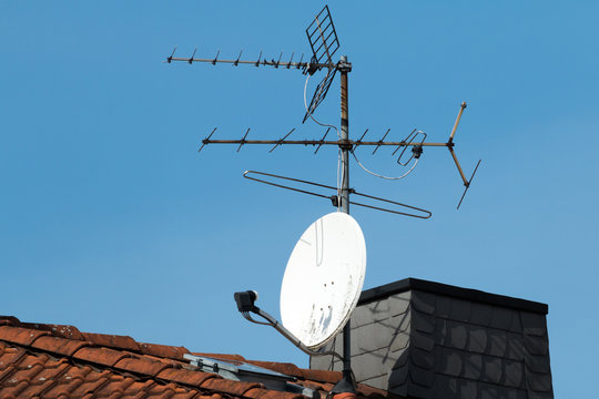 satellitenschüssel und alte antenne auf einem roten dach