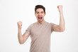 © Drobot Dean - Photo of delighted happy man 30s in casual t-shirt screaming and rejoicing his victory with clenched fists, isolated over white background