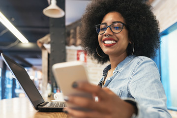 Beautiful afro american woman using mobile in the coffee shop.