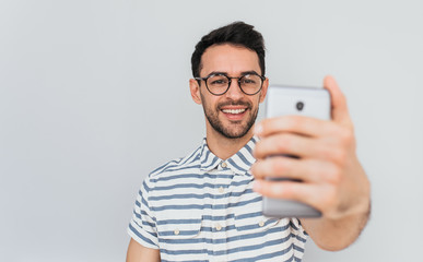 Sticker - Horizontal portrait of Caucasian male in stylish round glasses posing for selfie with happy smile, wearing blue striped shirt against white background. People, lifestyle and modern technology concept.