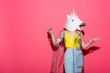 Wall Mural - funny woman in fashionable transparent raincoat and unicorn mask on red