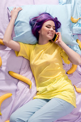 Wall Mural - high angle view of happy young woman lying in bed with bananas and talking by phone