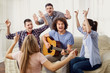 © Studio Romantic - A group of friends with a guitar sing fun songs at a party indoor.